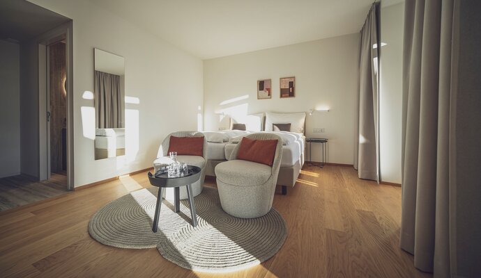 Helles Doppelzimmer mit Holzboden, Salontisch und Sitzgelegenheiten | © Davos Klosters Mountains 